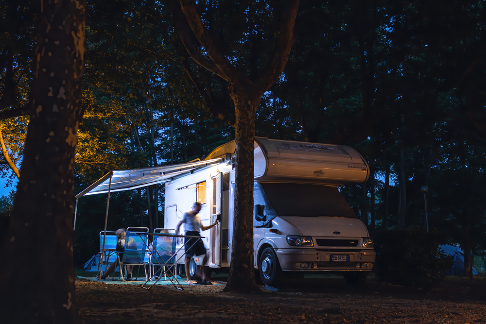 A White Rv Parked In A Wooded Area, Illuminated By External Camping Lights.